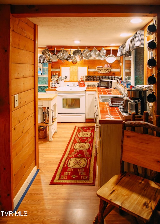 kitchen with beamed ceiling, log walls, light hardwood / wood-style floors, and white range with electric stovetop