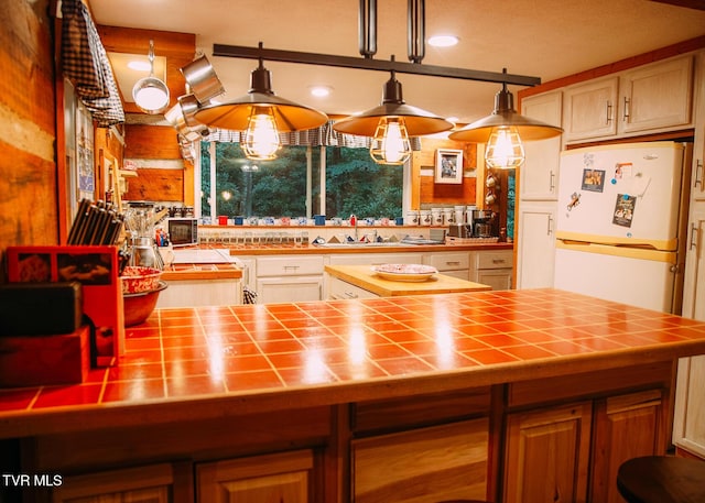 kitchen with pendant lighting, tile counters, sink, and white fridge