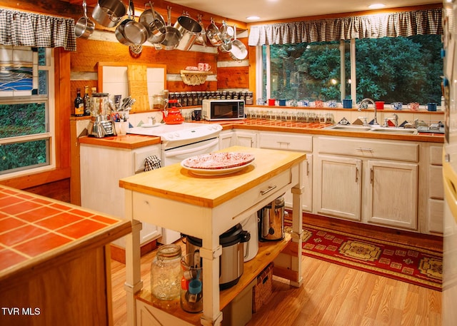 kitchen featuring sink, butcher block countertops, white electric stove, a kitchen island, and light hardwood / wood-style floors