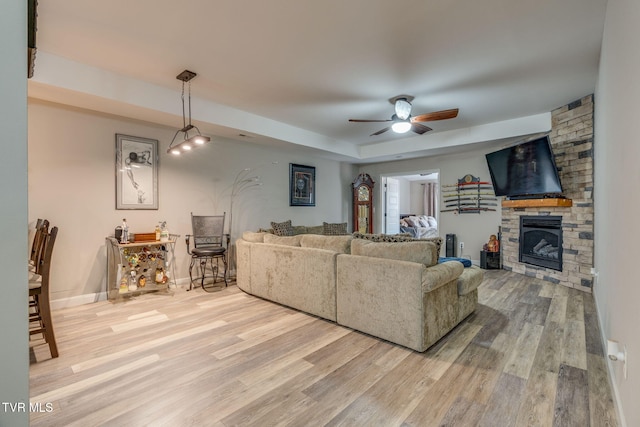 living room with ceiling fan, a fireplace, baseboards, and wood finished floors