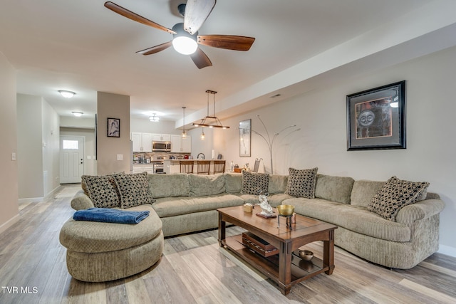 living room with a ceiling fan, light wood-type flooring, and baseboards