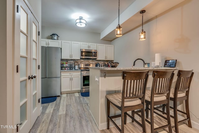 kitchen with tasteful backsplash, light wood-style flooring, a breakfast bar, a peninsula, and stainless steel appliances