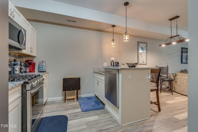 kitchen featuring stainless steel appliances, a peninsula, light wood-style floors, a kitchen breakfast bar, and light stone countertops