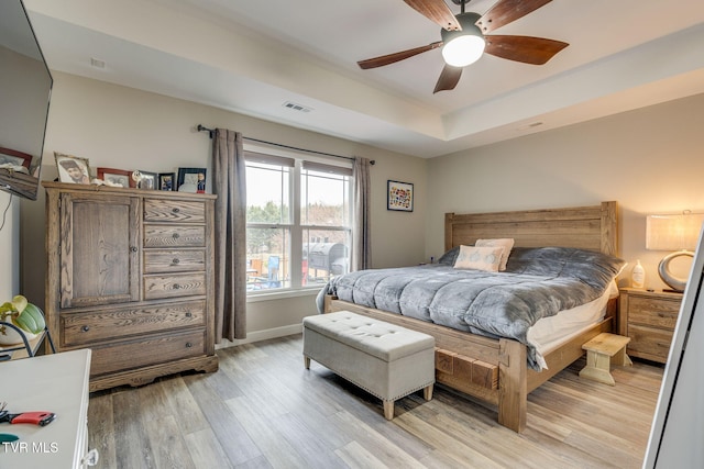 bedroom with a raised ceiling, visible vents, a ceiling fan, light wood-type flooring, and baseboards