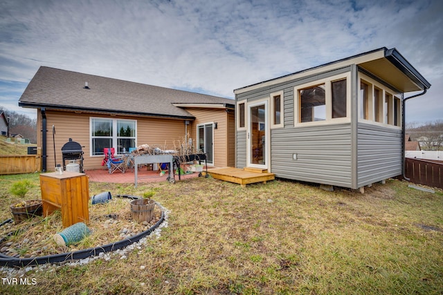 rear view of property featuring a shingled roof, a lawn, fence, and a wooden deck