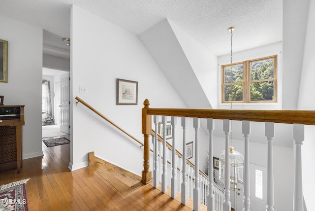 staircase with lofted ceiling, wood-type flooring, and a textured ceiling