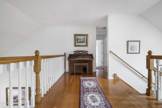 hallway with wood-type flooring, lofted ceiling, and a textured ceiling