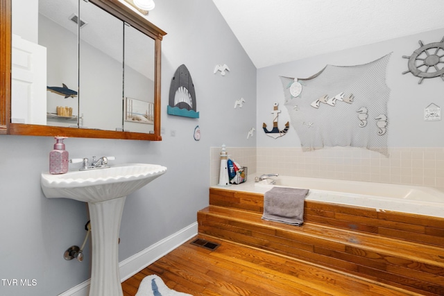 bathroom with wood-type flooring, a bath, and vaulted ceiling