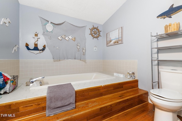 bathroom featuring a relaxing tiled tub, a textured ceiling, vaulted ceiling, and toilet