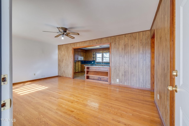 unfurnished living room with ceiling fan, wooden walls, and light hardwood / wood-style flooring