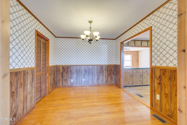 unfurnished dining area with ornamental molding, an inviting chandelier, and light wood-type flooring