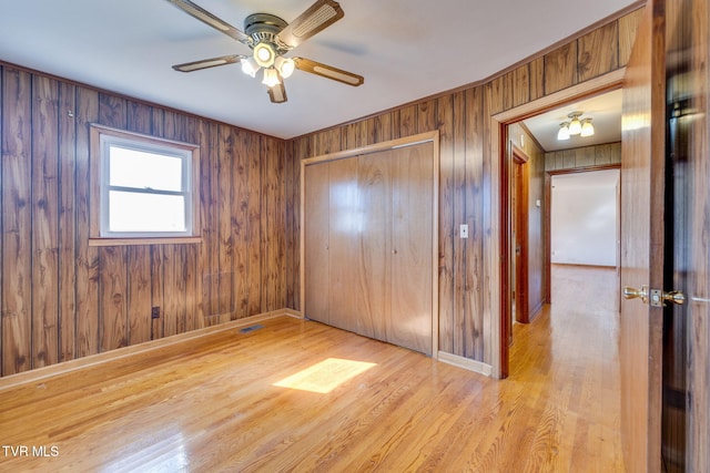 unfurnished bedroom with light hardwood / wood-style flooring, a closet, and wooden walls