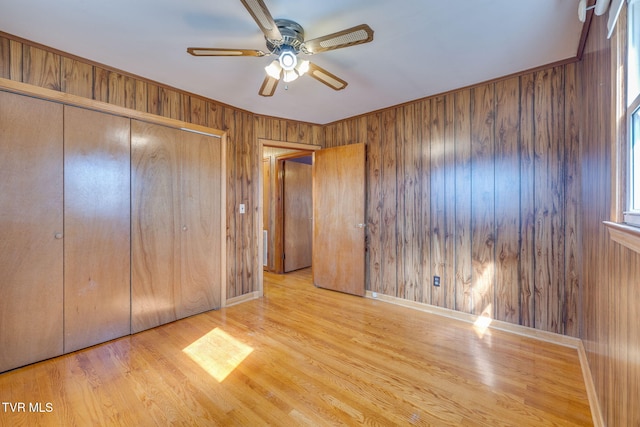 unfurnished bedroom featuring light hardwood / wood-style floors, a closet, ceiling fan, and wood walls