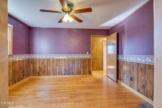 empty room featuring ceiling fan, wooden walls, and light hardwood / wood-style flooring