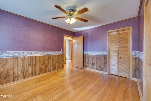 unfurnished bedroom with crown molding, a closet, ceiling fan, and light wood-type flooring