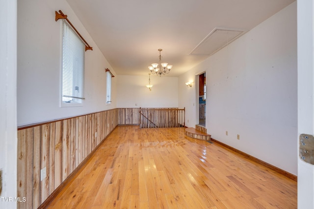 empty room with wood-type flooring, an inviting chandelier, and wooden walls