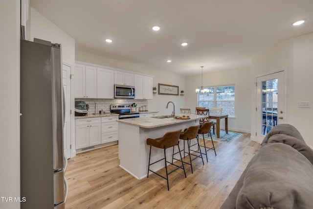 kitchen with pendant lighting, a kitchen island with sink, stainless steel appliances, light hardwood / wood-style floors, and white cabinets