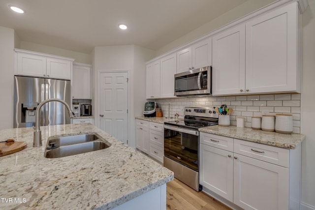 kitchen featuring sink, white cabinetry, light stone counters, appliances with stainless steel finishes, and backsplash