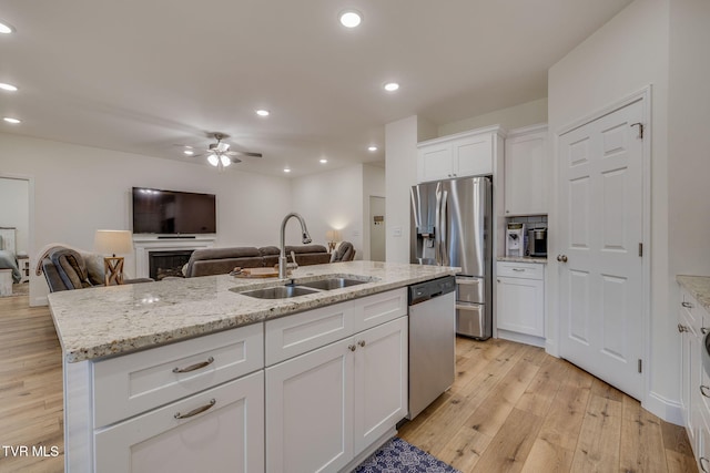 kitchen featuring sink, light stone counters, stainless steel appliances, a kitchen island with sink, and white cabinets