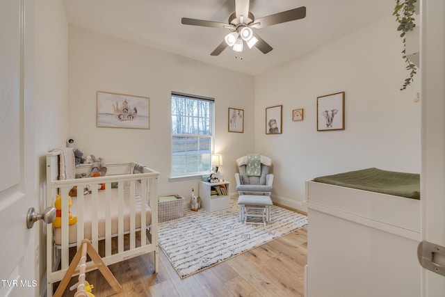 bedroom featuring a nursery area, ceiling fan, and light hardwood / wood-style flooring