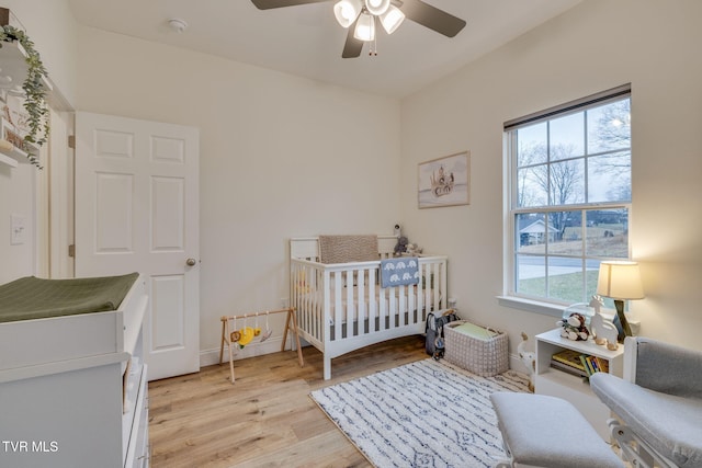 bedroom with ceiling fan, light wood-type flooring, and a crib