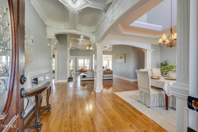 foyer entrance featuring decorative columns, ornamental molding, a notable chandelier, and light hardwood / wood-style floors