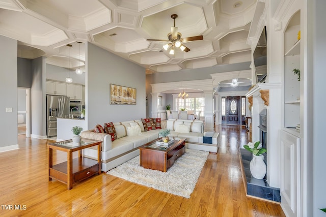 living room featuring a high ceiling, decorative columns, ceiling fan, and light wood-type flooring