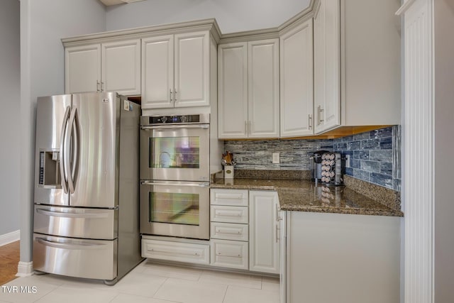 kitchen featuring backsplash, stainless steel appliances, light tile patterned floors, and dark stone countertops