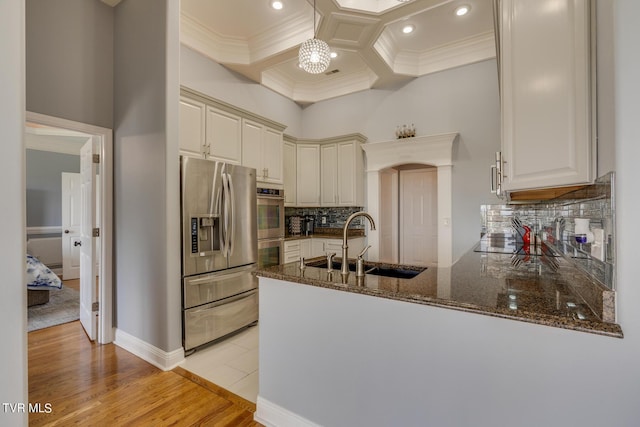 kitchen with coffered ceiling, sink, appliances with stainless steel finishes, kitchen peninsula, and dark stone counters