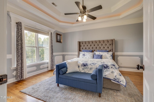 bedroom featuring a raised ceiling, crown molding, ceiling fan, and light wood-type flooring