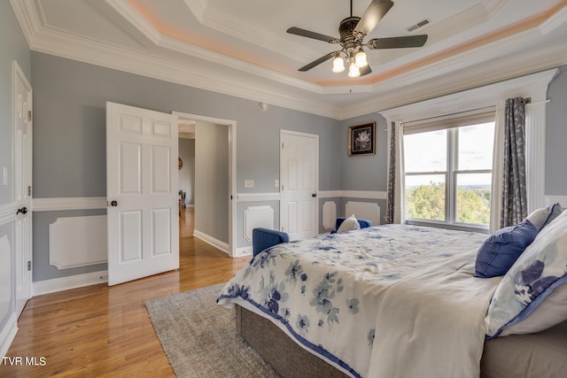 bedroom featuring crown molding, light hardwood / wood-style flooring, ceiling fan, and a tray ceiling