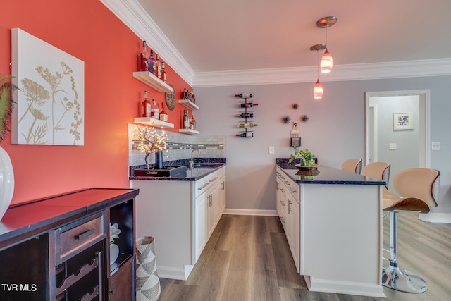 kitchen with crown molding, a breakfast bar area, hardwood / wood-style floors, white cabinets, and decorative backsplash