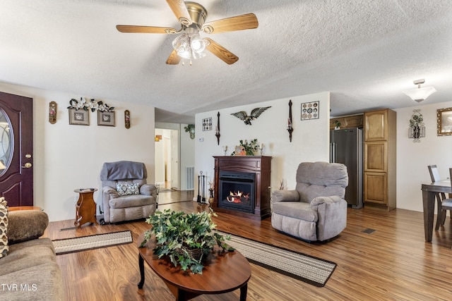 living room featuring ceiling fan, light hardwood / wood-style flooring, and a textured ceiling