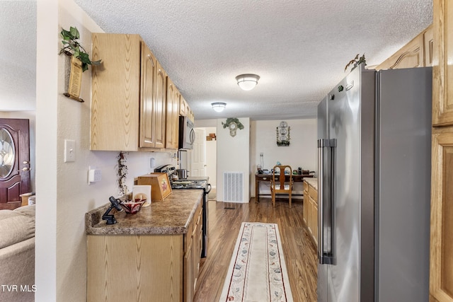 kitchen with appliances with stainless steel finishes, dark hardwood / wood-style floors, light brown cabinetry, and a textured ceiling