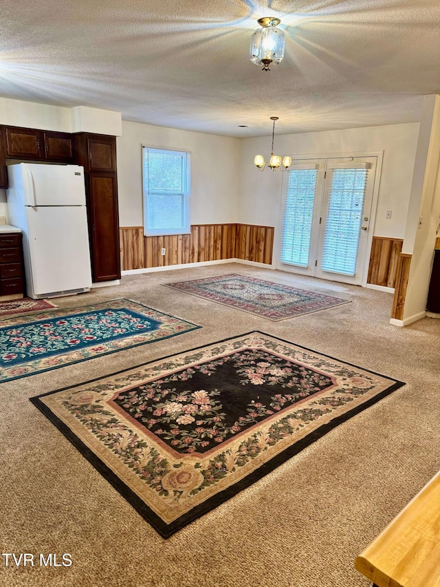 entryway featuring carpet flooring, a chandelier, a textured ceiling, and wood walls