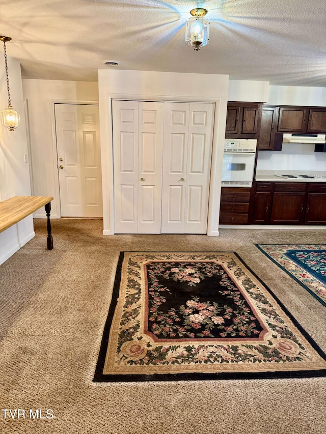 kitchen with dark brown cabinetry, decorative light fixtures, light carpet, a textured ceiling, and white appliances