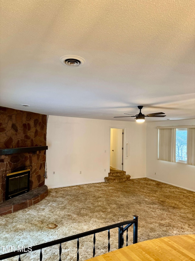 living room with ceiling fan, a stone fireplace, carpet floors, and a textured ceiling