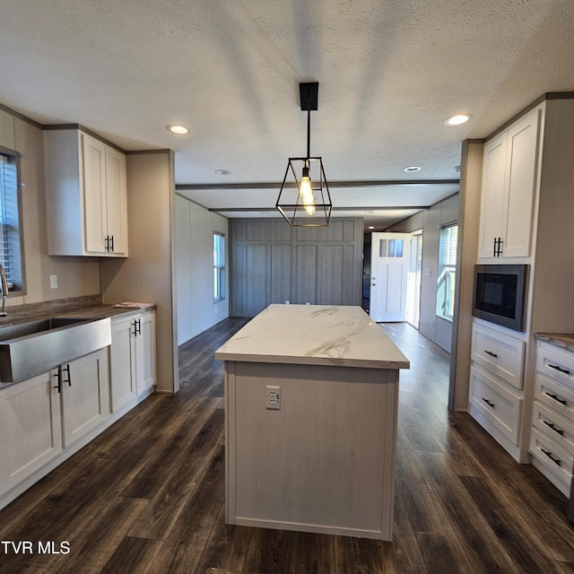 kitchen featuring sink, hanging light fixtures, black microwave, a textured ceiling, and white cabinets