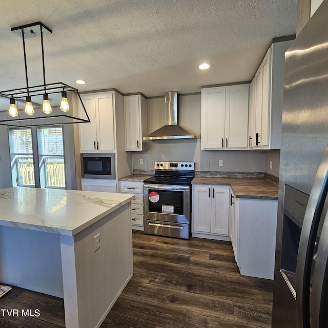 kitchen with dark wood-type flooring, stainless steel appliances, white cabinets, decorative light fixtures, and wall chimney exhaust hood