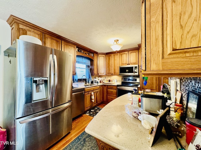 kitchen featuring sink, a tile fireplace, appliances with stainless steel finishes, light hardwood / wood-style floors, and a textured ceiling