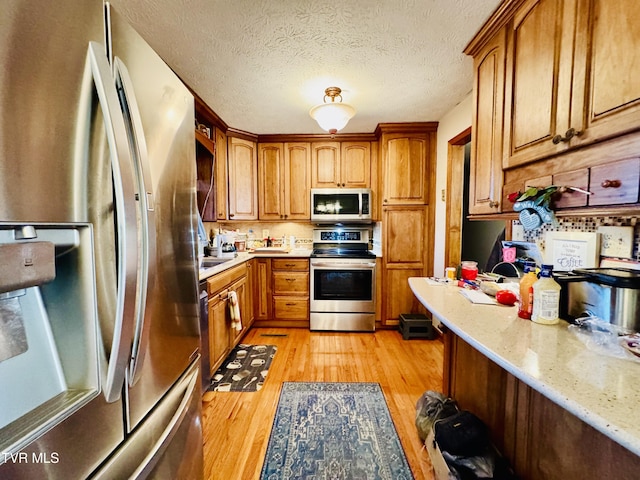 kitchen featuring light stone countertops, stainless steel appliances, a textured ceiling, and light wood-type flooring