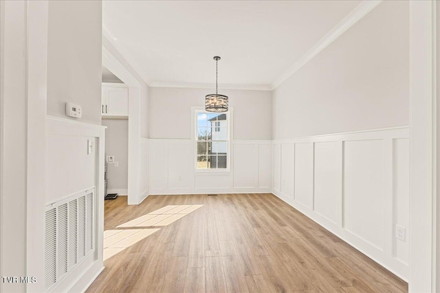 unfurnished dining area featuring ornamental molding, an inviting chandelier, and light hardwood / wood-style floors