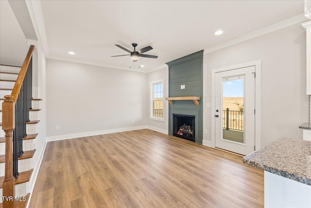 unfurnished living room featuring crown molding, a large fireplace, ceiling fan, and light hardwood / wood-style flooring