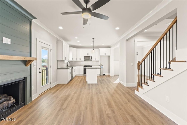 living room with ornamental molding, a large fireplace, sink, and light hardwood / wood-style flooring