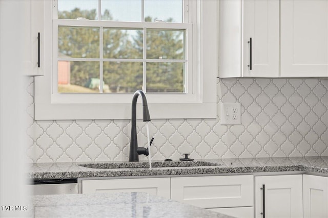 kitchen with light stone counters, sink, tasteful backsplash, and white cabinets