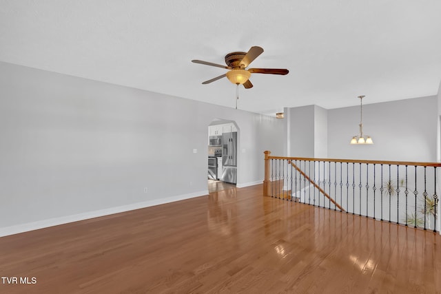 spare room featuring ceiling fan with notable chandelier and hardwood / wood-style floors