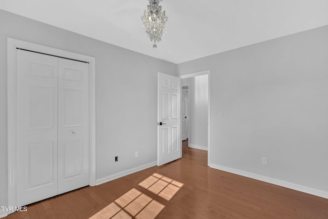 unfurnished bedroom featuring a notable chandelier, hardwood / wood-style flooring, and a closet