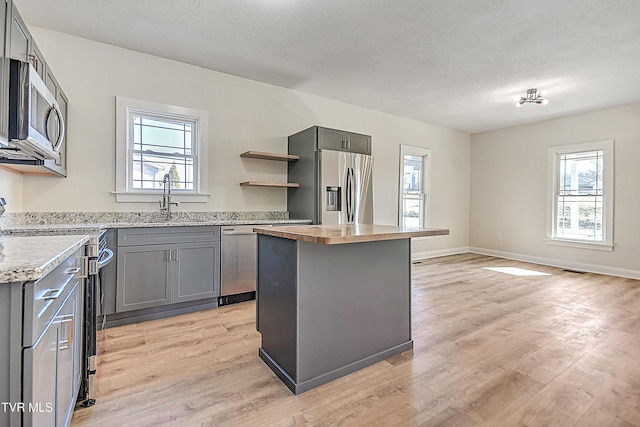 kitchen with a kitchen island, a healthy amount of sunlight, gray cabinetry, and appliances with stainless steel finishes