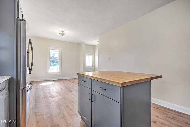 kitchen with butcher block countertops, stainless steel refrigerator, gray cabinetry, a kitchen island, and light wood-type flooring