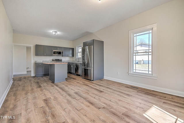 kitchen with gray cabinets, stainless steel appliances, a center island, and light wood-type flooring